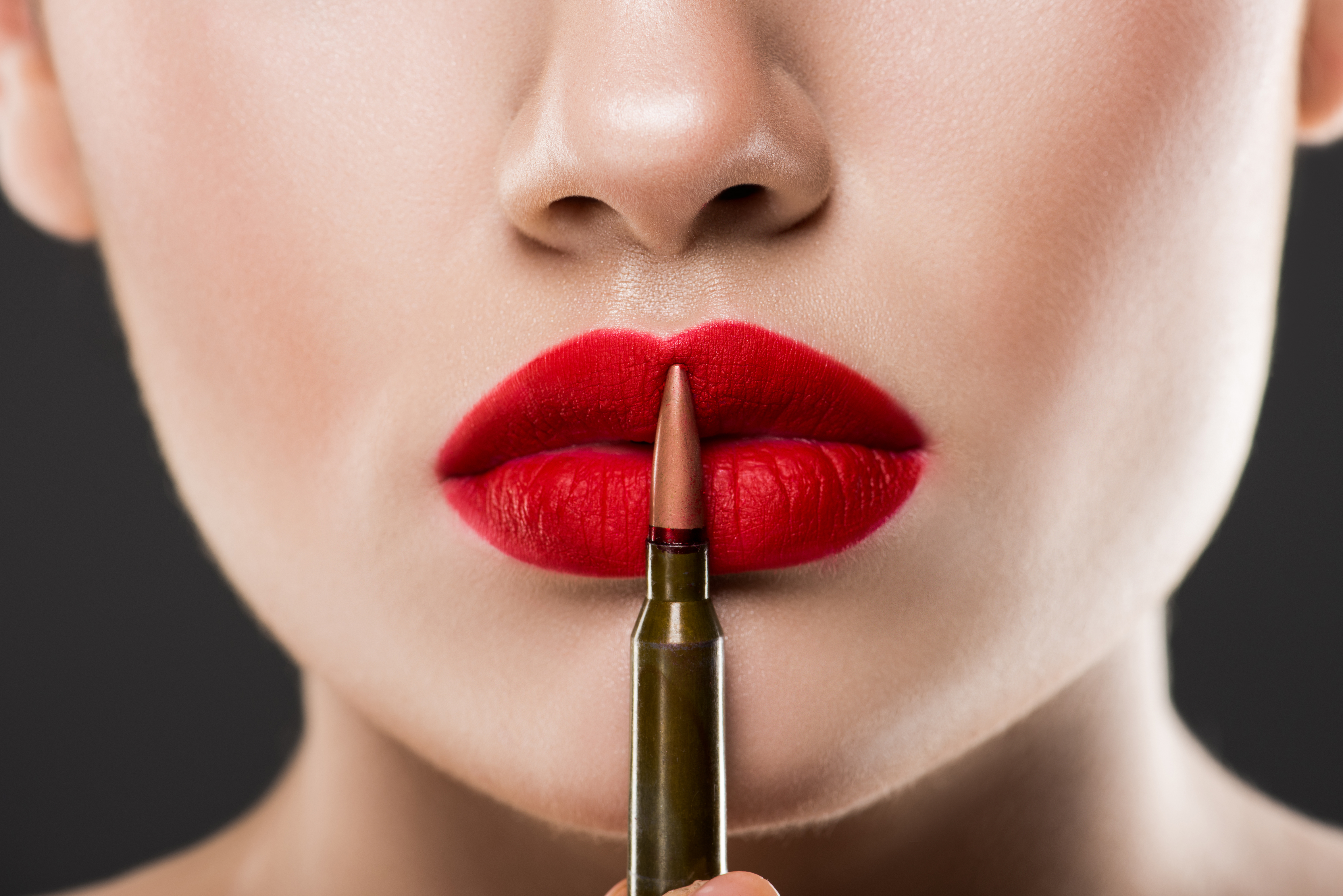 partial view of young woman holding bullet near red lips, isolated on grey